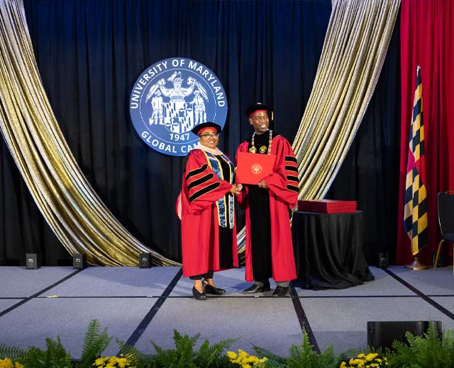 A UMGC graduate receiving a diploma on stage on graduation day.