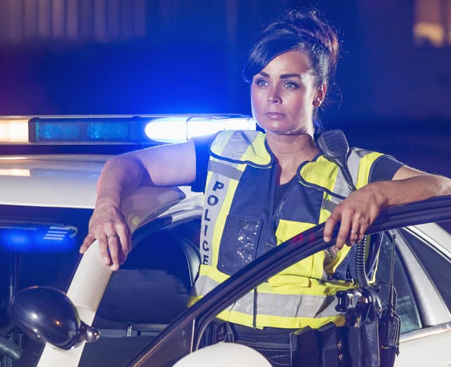 A police officer in a bright safety vest standing next to a police vehicle.