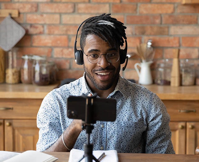 A person wearing headphones smiling and video chatting with someone on their phone.