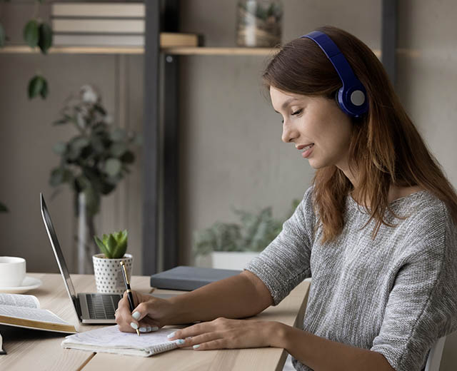 A person wearing headphones and writing in a notebook.