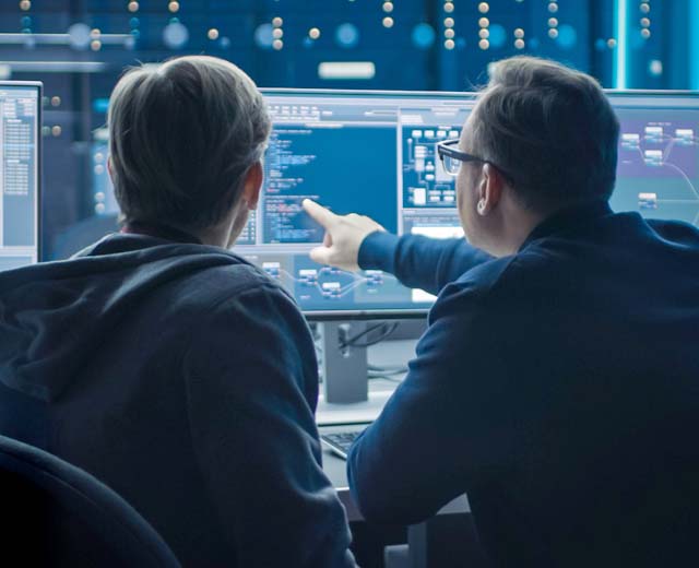 Two men looking at a computer screen doing programming.