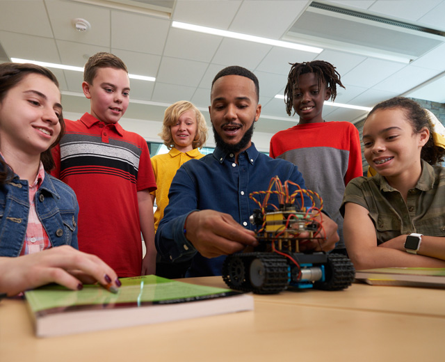 An adult plays with a toy vehicle while several children look on.