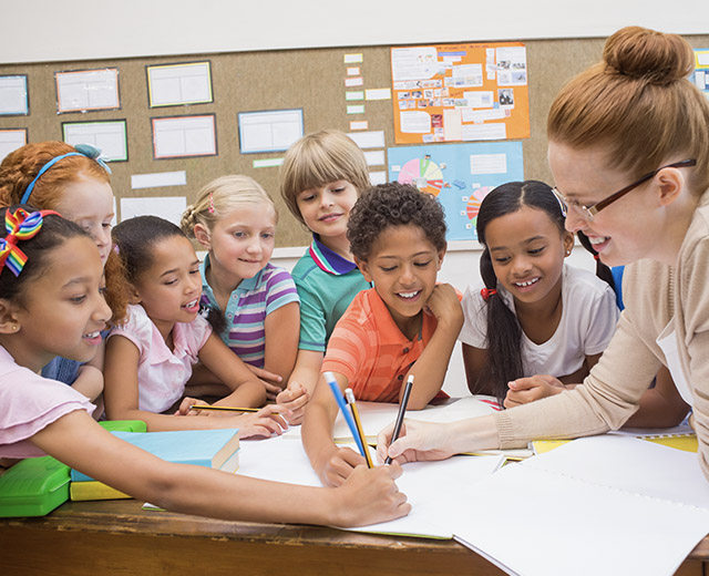 Students sitting around a table smiling watching an adult write in a notebook.