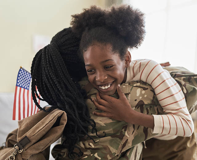 A person in a military uniform hugging a child.