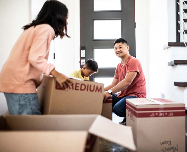A man and woman pack moving boxes while a child sits in the background.