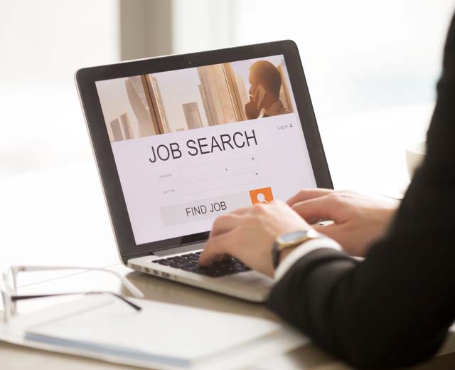 A person's hands on a laptop with the words "Job Search" on the screen.