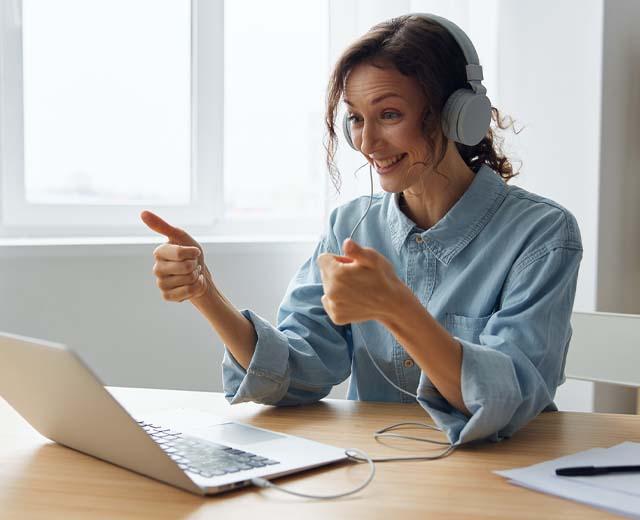 A person sitting at a desk with a laptop giving a thumbs up sign.