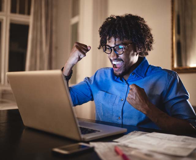 A person cheering with joy and looking at a laptop screen.