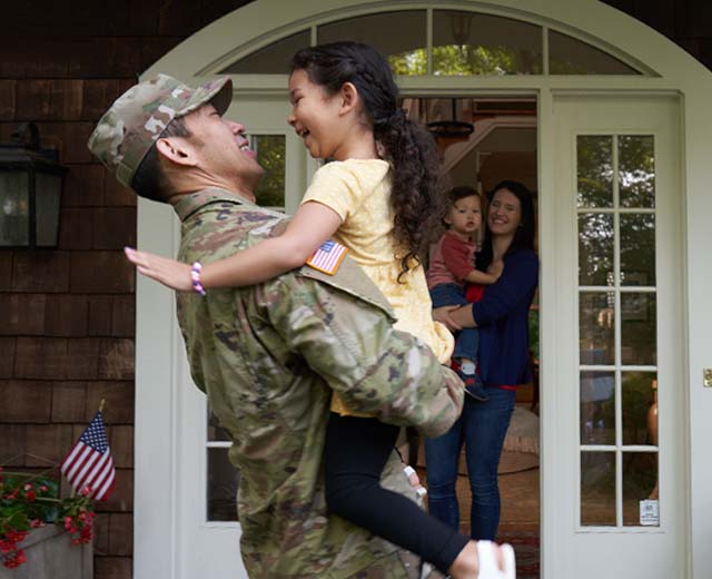 A person in a military uniform hugging a young child.