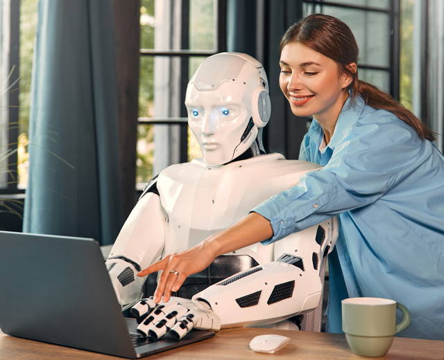 A person and a robot working on a laptop together.