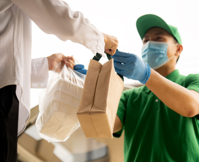 A food delivery person in a mask hands the delivery bags to a customer.