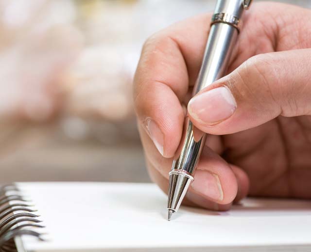 Close up of a person's hand holding a pen and writing in a notebook.