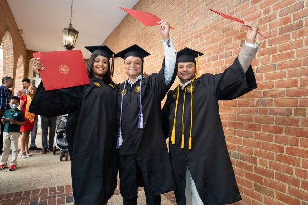 Three graduates raising their folios in celebration.