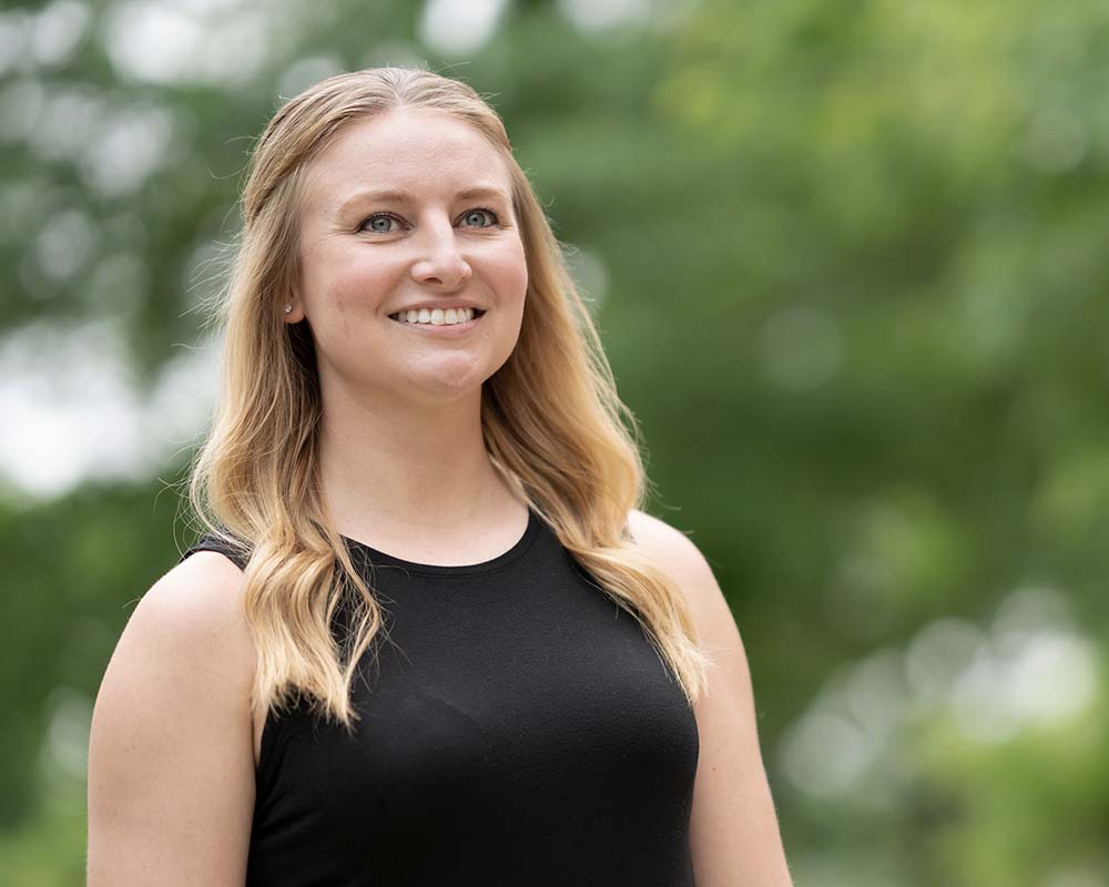 A UMGC graduate in professional clothing smiling in an outdoor location.