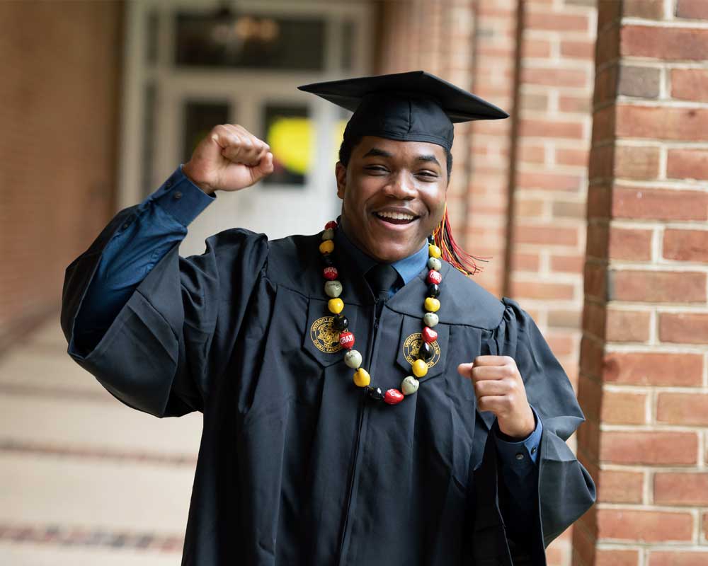 A student in graduation regalia cheering.