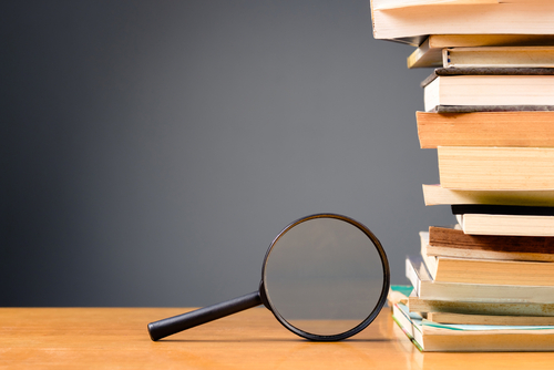 Magnifying glass and pile of books on the wood desk with copy space