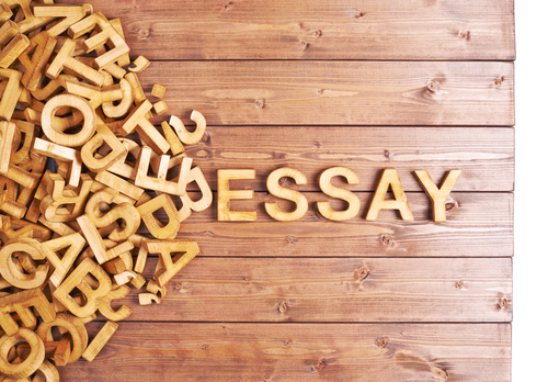 Word essay made with block wooden letters next to a pile of other letters over the wooden board surface composition