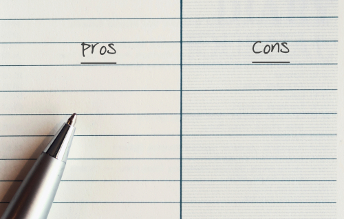 A silver pen on a line note paper with text written PROS and  CONS - concept of making decision by listing  its advantages and disadvantages to consider and compare before making a decision