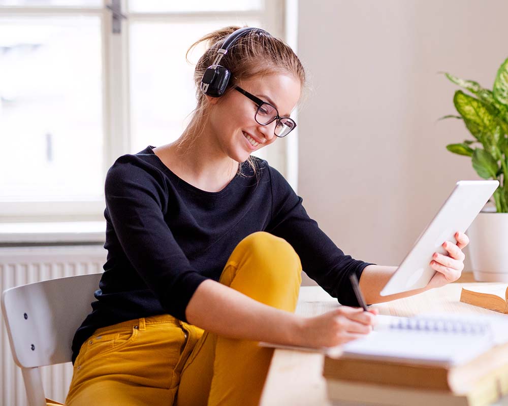 A person with headphones on smiling and writing in a notebook.