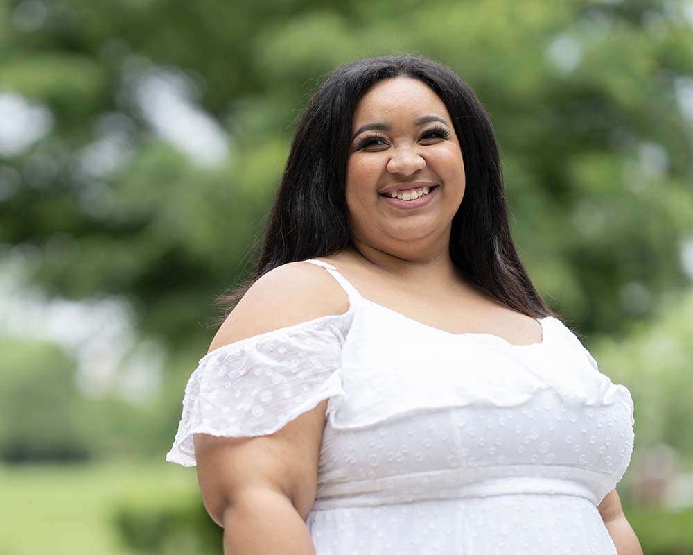 A UMGC graduate in professional clothing smiling in an outdoor location.