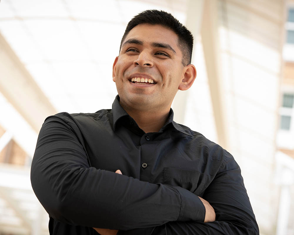 A UMGC Graduate at work with his arms crossed and smiling.