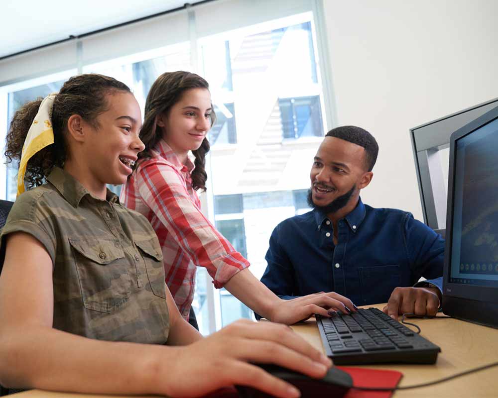 A teacher and two students are looking at something on a computer.