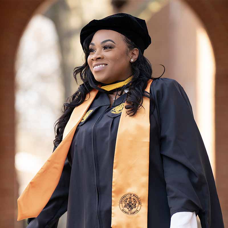 A UMGC graduate in graduation regalia smiling.