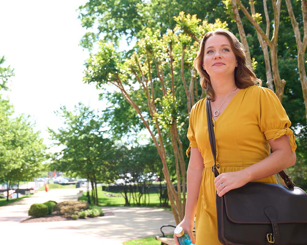 A person outside holding a laptop bag and smiling.