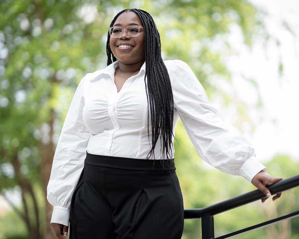 A UMGC graduate standing with one hand on a railing outside smiling.