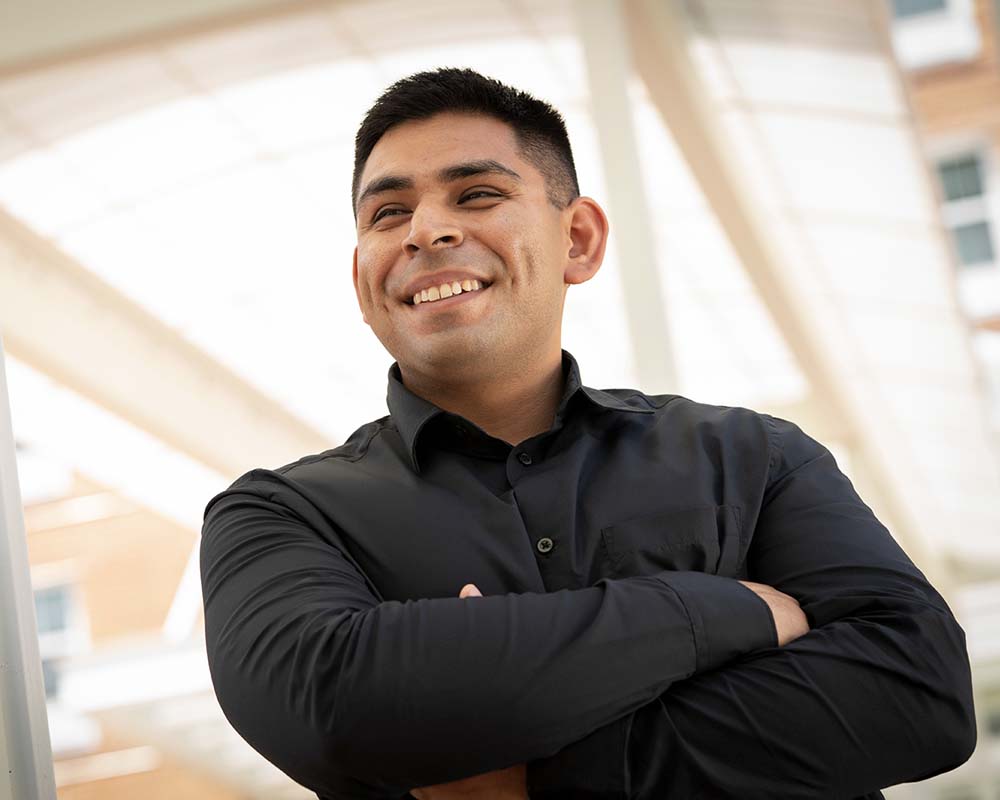 A UMGC graduate in professional clothing smiling and crossing their arms.