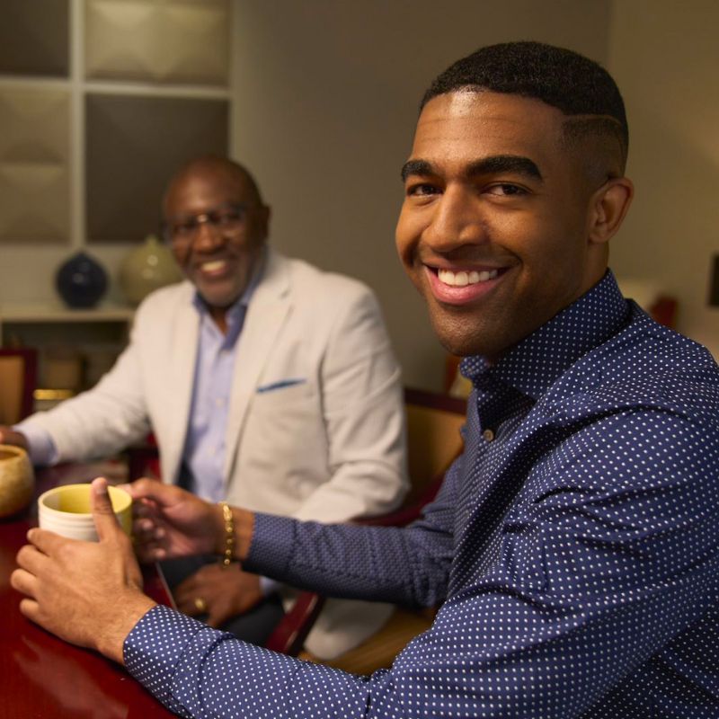 Two people having coffee, looking at the camera, and smiling.