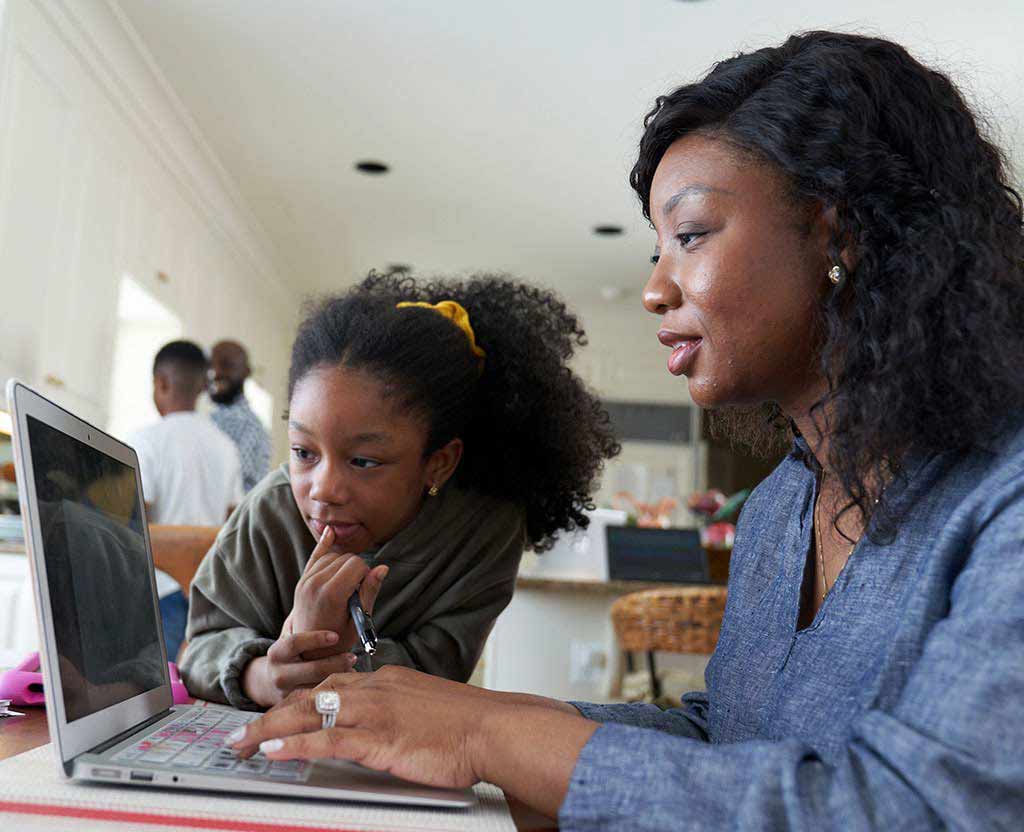 A UMGC MBA student working on a laptop while a child looks on.