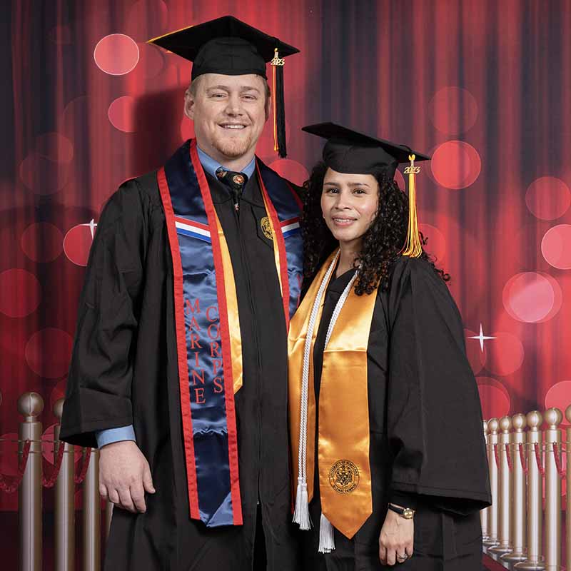 Two UMGC graduates in graduation regalia smiling.