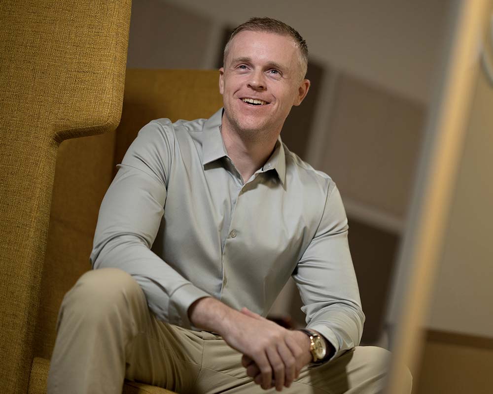 A UMGC graduate in professional clothing sitting and smiling.