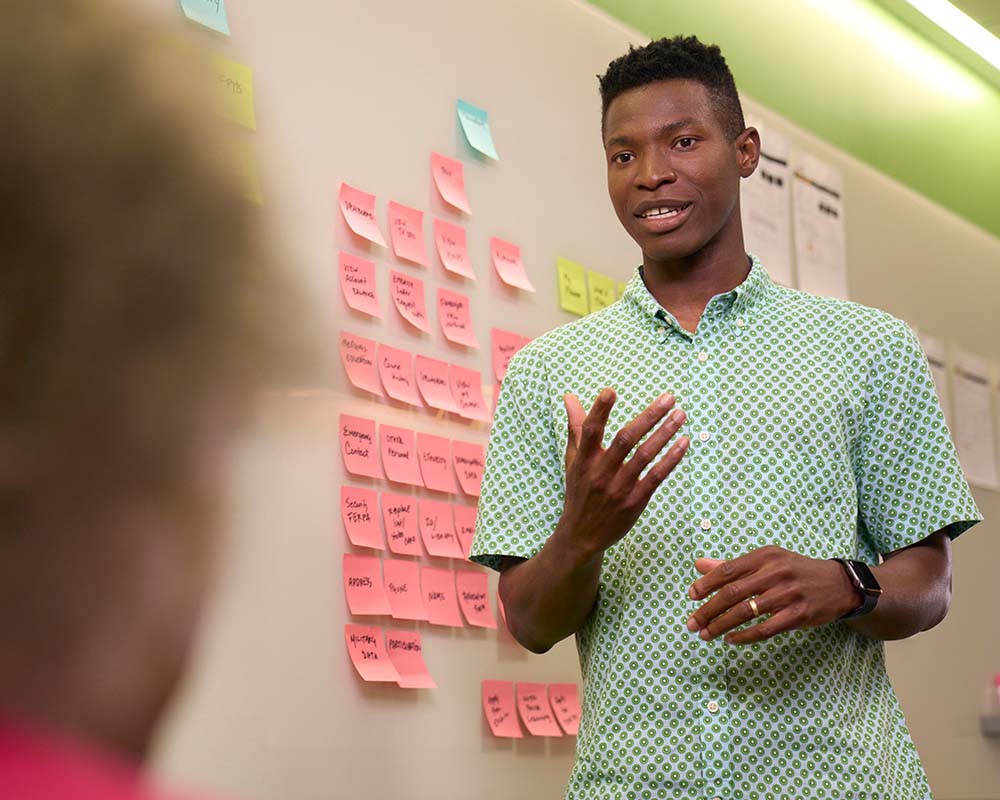 A person standing in front of a whiteboard with sticky notes on it.