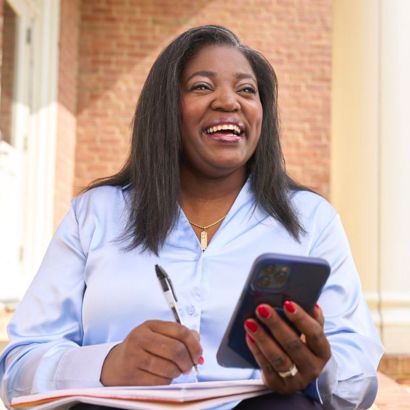 A person smiling and taking notes while holding a cell phone.