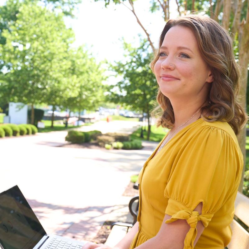 A person smiling with a laptop on their lap outside.