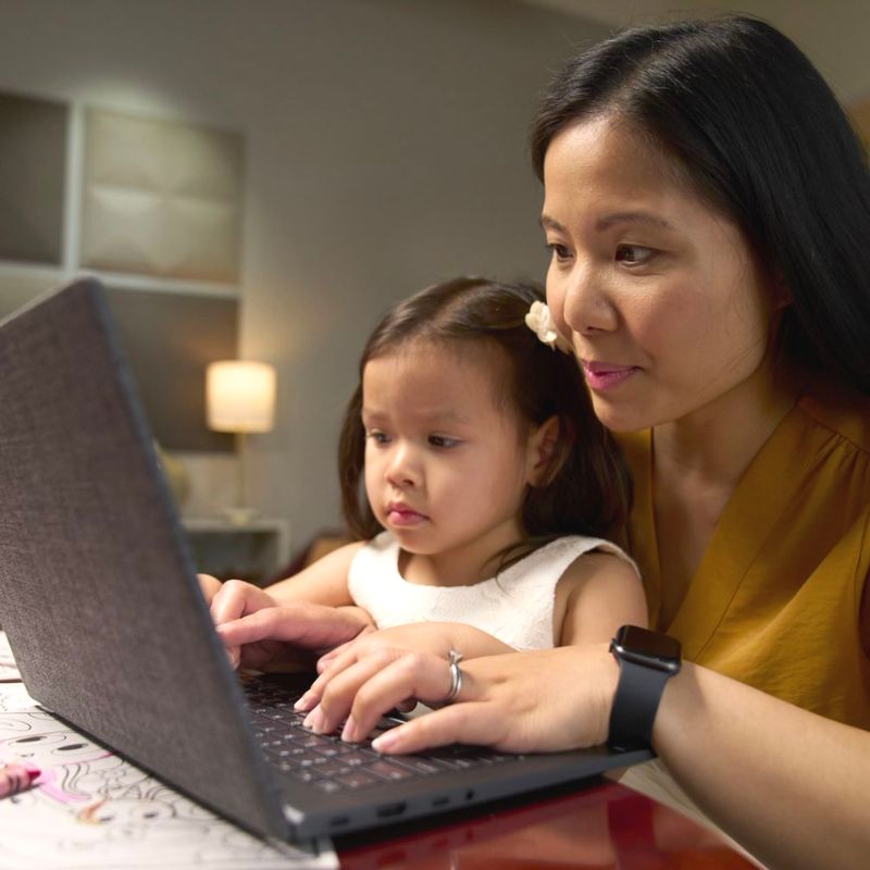 A person typing on a laptop with a child in their lap.