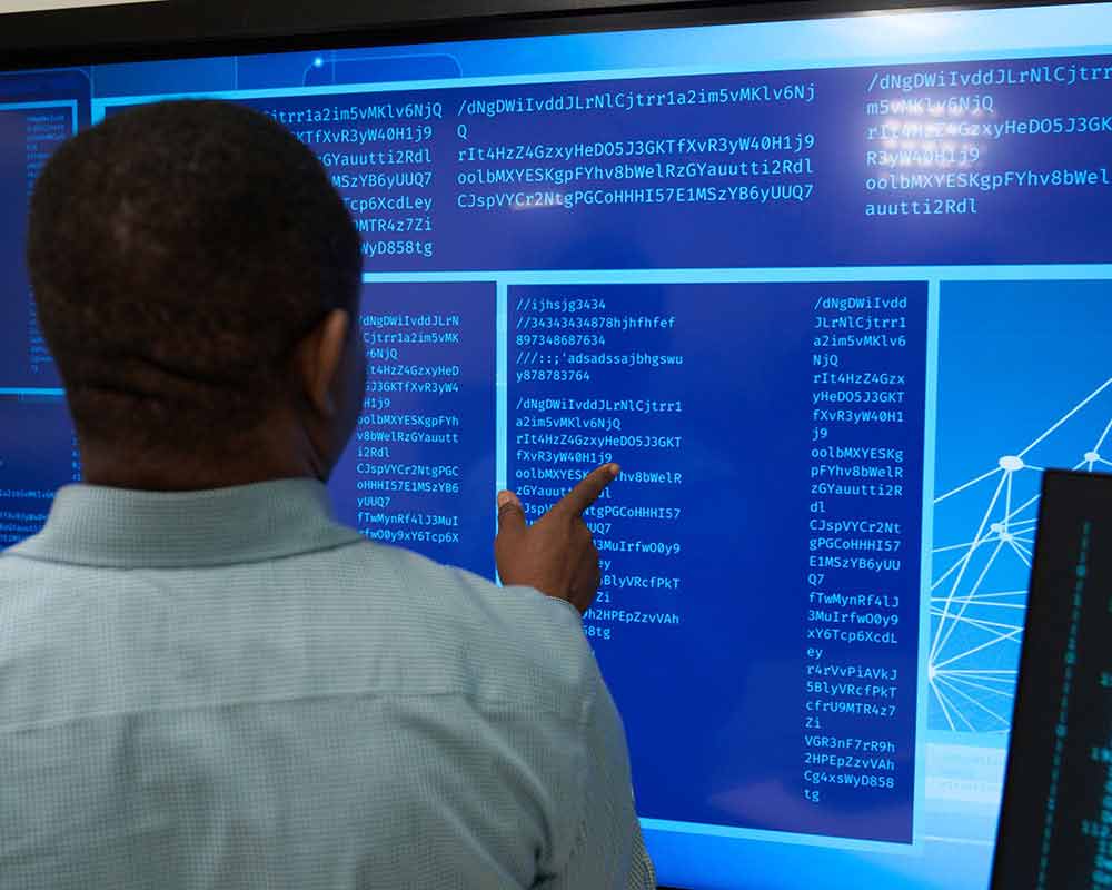 A UMGC student, who is pursuing a master's degree in information assurance, is looking at data on a large screen.