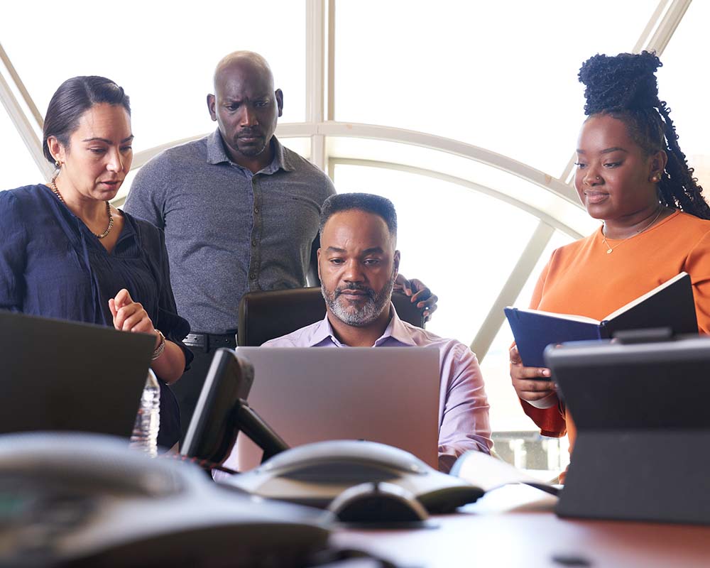 A group of people looking on as another person types on a laptop.