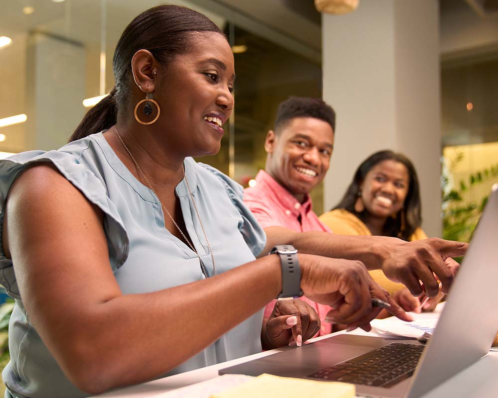 Three people smiling while looking at a laptop.