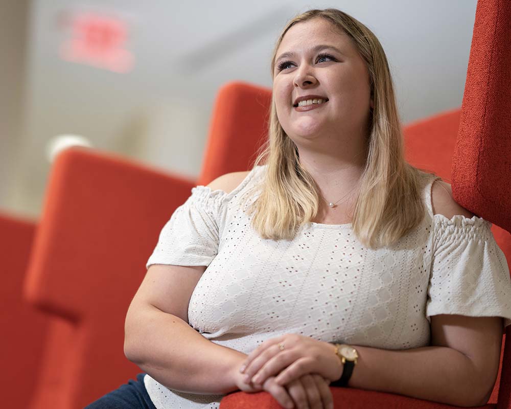 A UMGC graduate in professional clothing sitting and smiling.