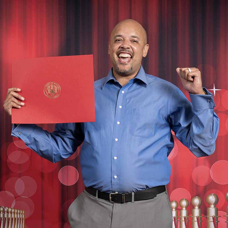 A UMGC graduate smiling and holding a diploma.