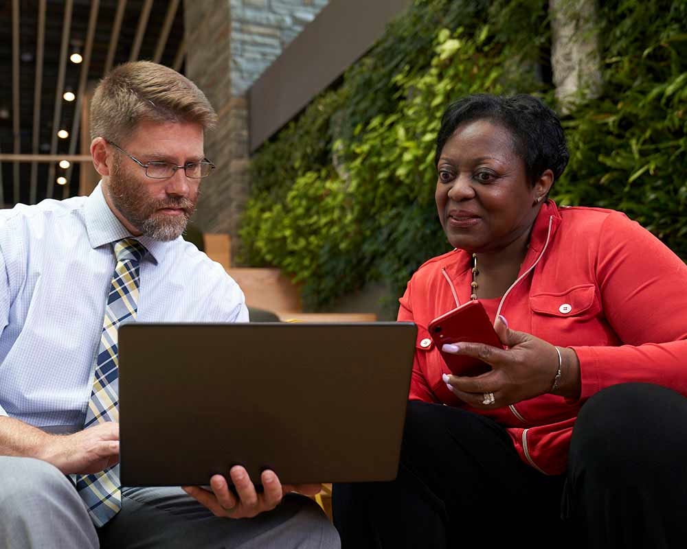 A UMGC student, who is pursuing a bachelor’s degree in human resources management, is looking at something on a laptop that another person is showing them. 