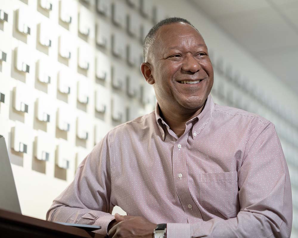 A UMGC graduate in professional clothing smiling and sitting at a table with a laptop.