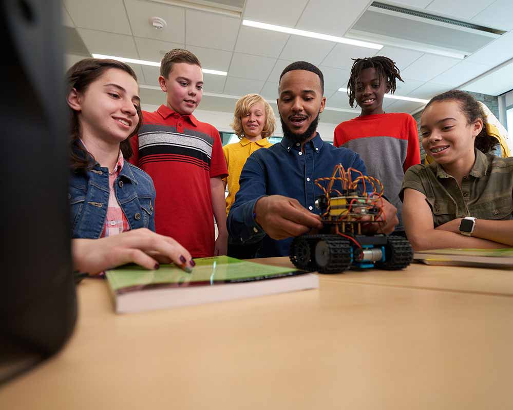 A teacher is showing their students a small robotic truck.