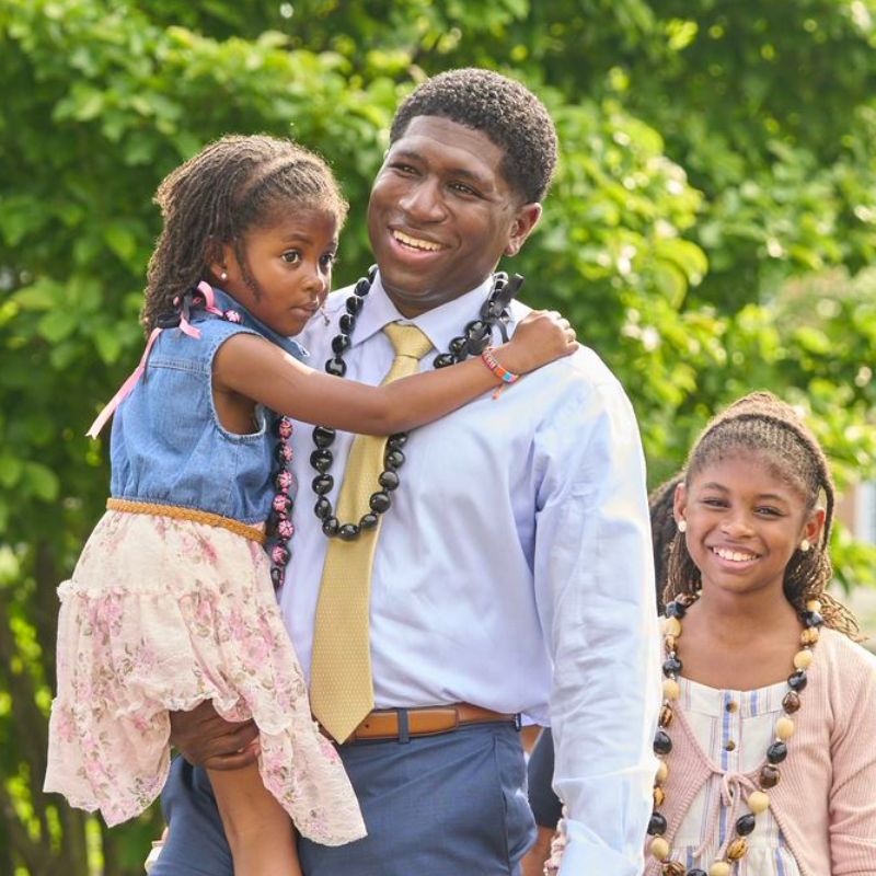 An adult holding a child with another child standing next to them.