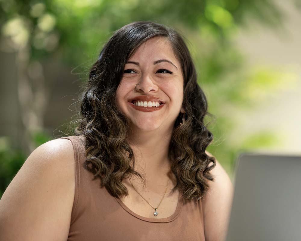 A UMGC graduate smiling in an outdoor location with a laptop.