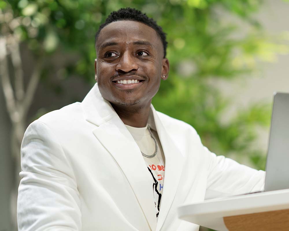 A UMGC graduate in professional clothing smiling in an outdoor location with a laptop.