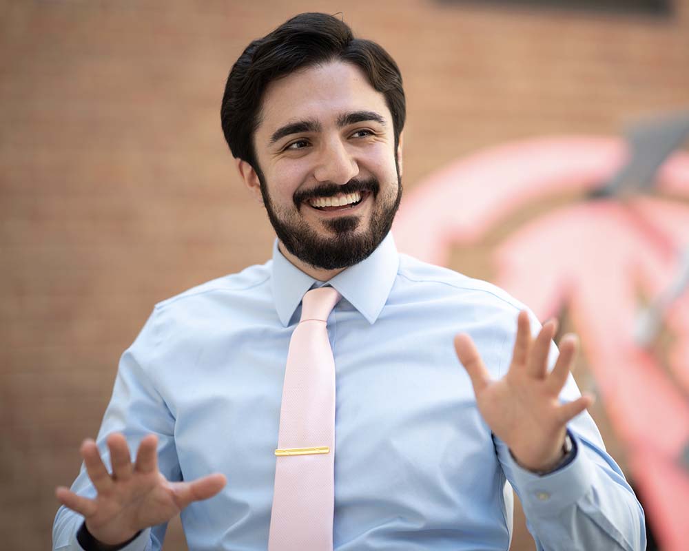 A UMGC graduate in professional clothing smiling and talking with their hands.